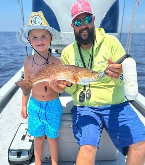 A boy and his dad holding a red fish.