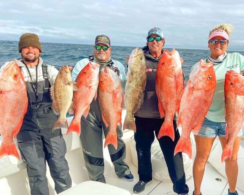 A group holding a their catch of Red Snapper and a Grouper.